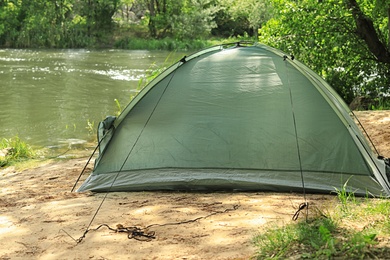Photo of Modern camping tent on riverbank in wilderness
