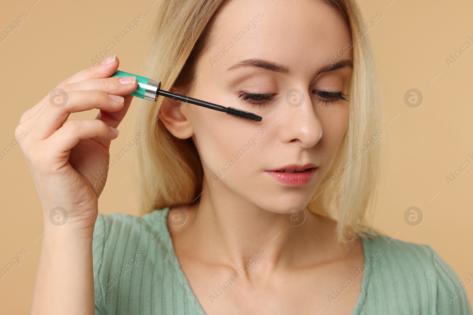 Photo of Beautiful woman applying mascara on beige background, closeup