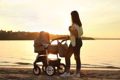 Happy mother with baby in stroller walking near river at sunset