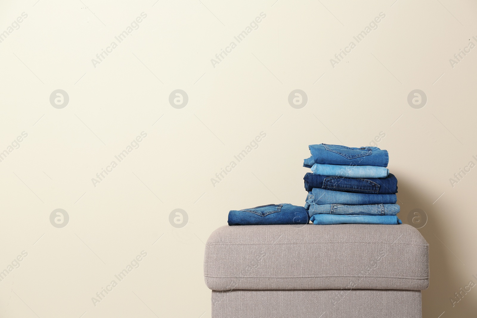 Photo of Stack of different jeans on ottoman against light background. Space for text