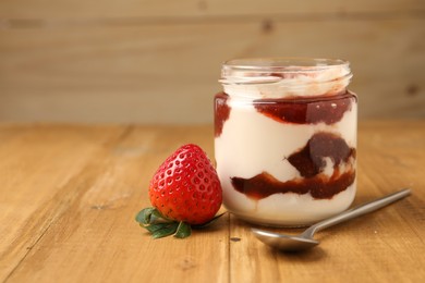 Photo of Tasty yoghurt with jam, spoon and strawberry on wooden table, closeup. Space for text