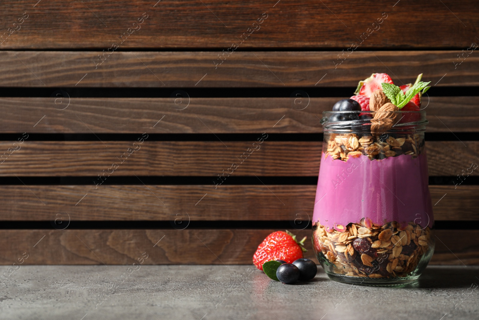 Photo of Delicious acai dessert with granola and berries in glass jar on grey table. Space for text