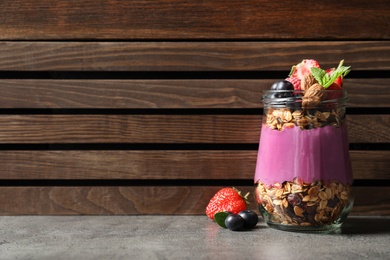 Photo of Delicious acai dessert with granola and berries in glass jar on grey table. Space for text