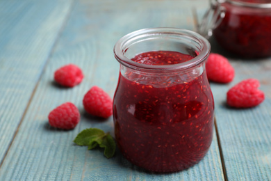 Photo of Delicious jam and fresh raspberries on light blue wooden table, closeup