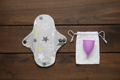 Photo of Reusable cloth pad and menstrual cup on wooden table, flat lay
