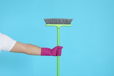 Photo of Young man with green broom on light blue background, closeup