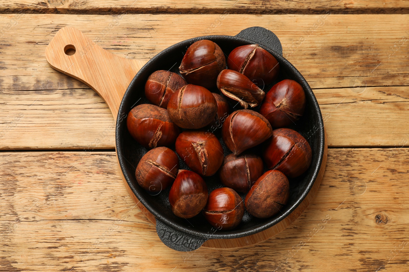 Photo of Fresh edible sweet chestnuts in frying pan on wooden table, top view