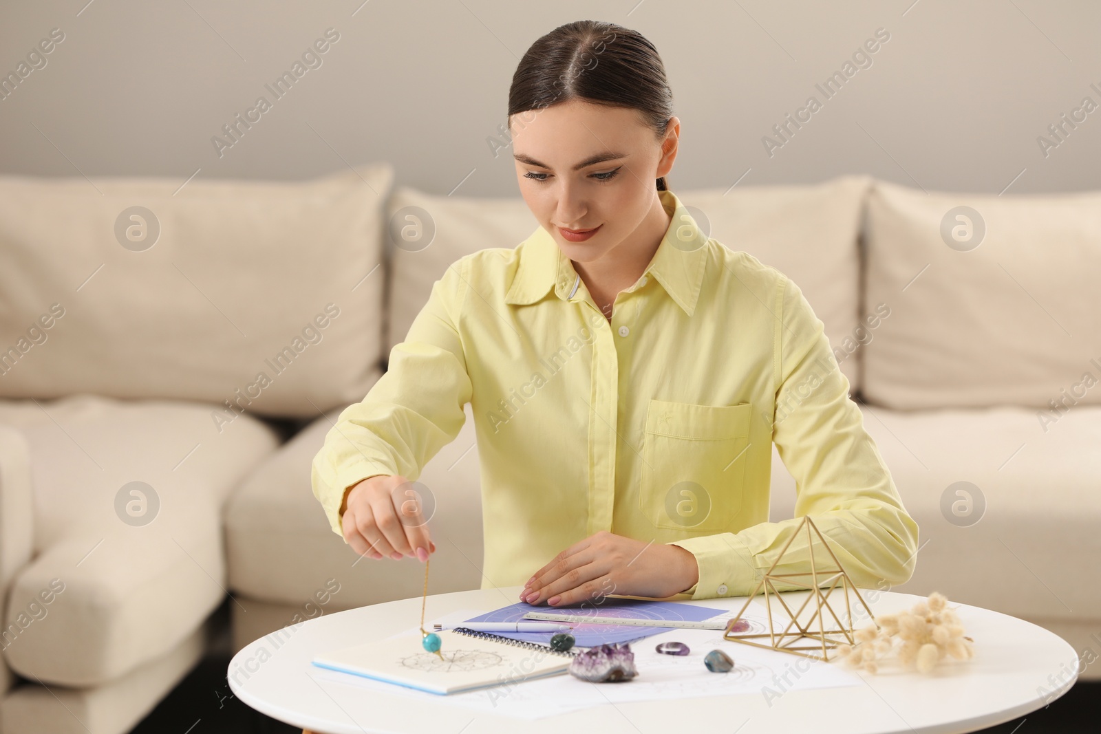 Photo of Astrologer using pendulum and zodiac wheel for fate forecast at table indoors. Fortune telling