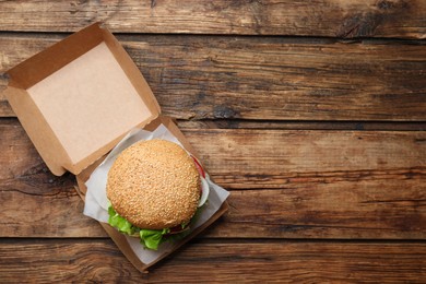 Photo of Delicious burger in cardboard box on wooden table, top view. Space for text