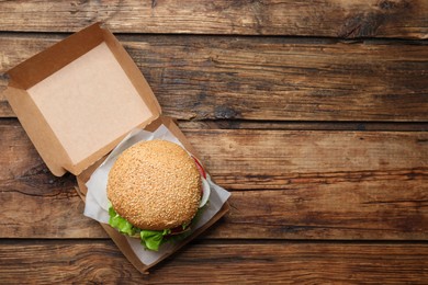 Delicious burger in cardboard box on wooden table, top view. Space for text