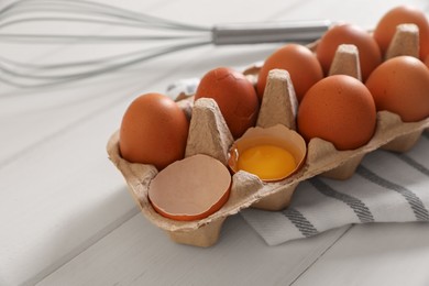 Photo of Fresh raw chicken eggs and whisk on white wooden table, closeup