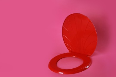 Photo of New red plastic toilet seat on pink background, space for text