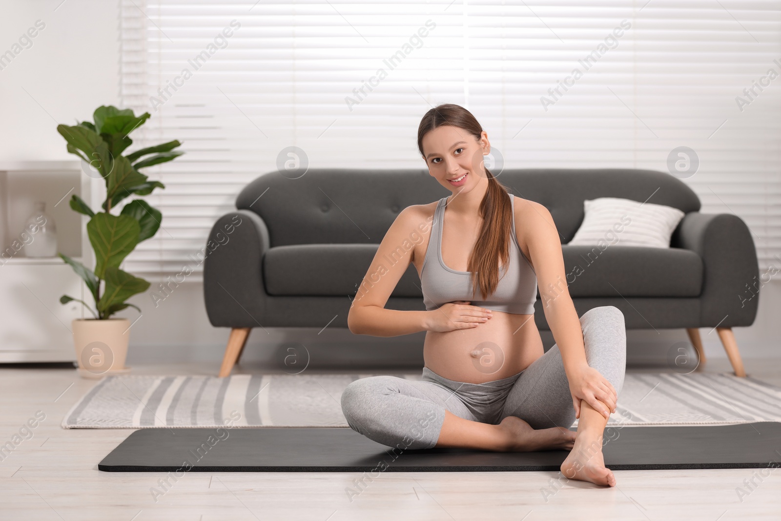 Photo of Pregnant woman sitting on yoga mat at home, space for text