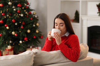 Woman drinking tea on sofa near Christmas tree at home