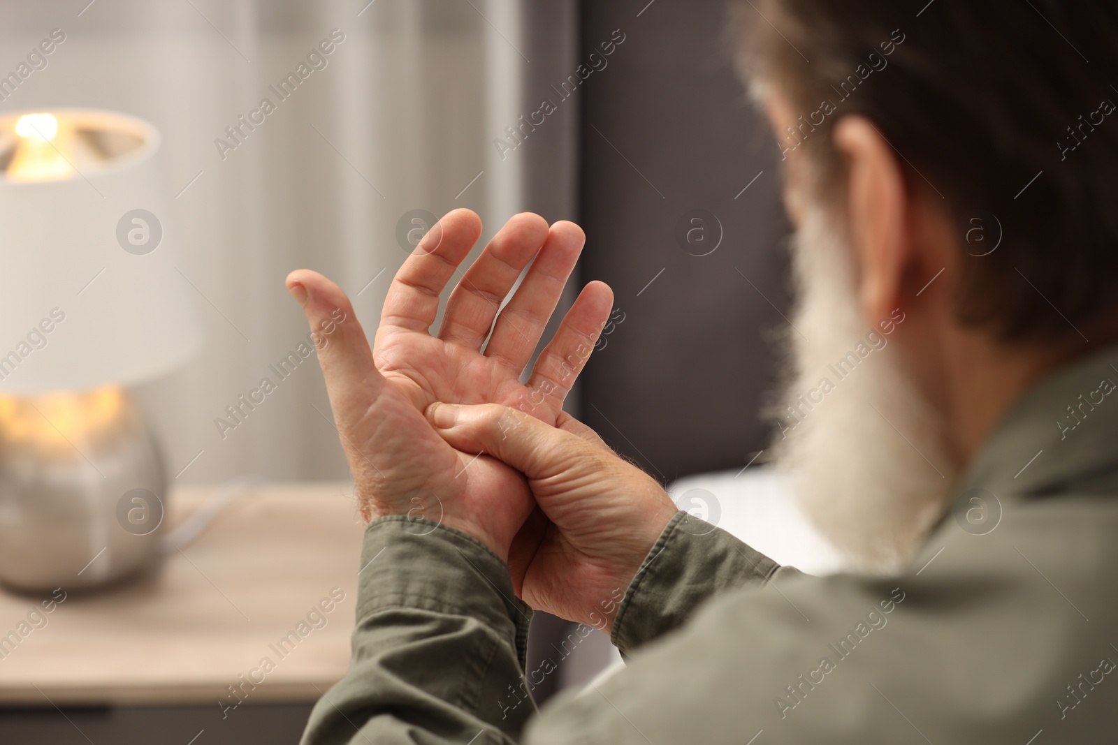 Photo of Senior man suffering from pain in hand at home, closeup. Rheumatism symptom