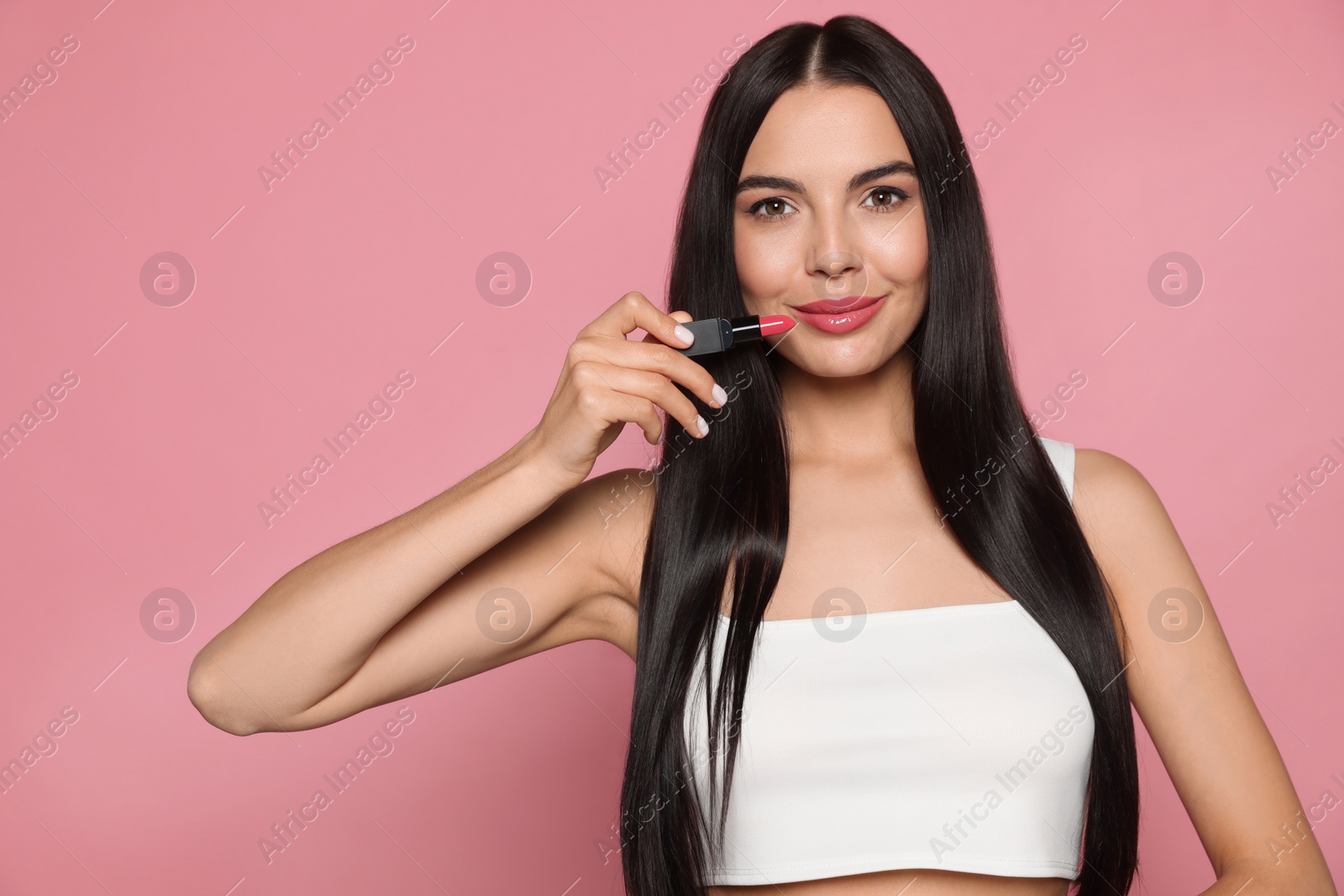 Photo of Young woman with beautiful makeup holding glossy lipstick on pink background