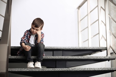 Sad little boy sitting on stairs indoors