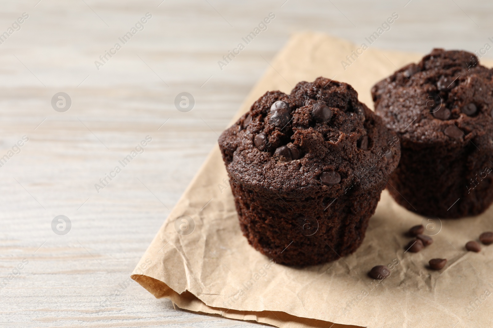 Photo of Delicious chocolate muffins on light wooden table, closeup. Space for text