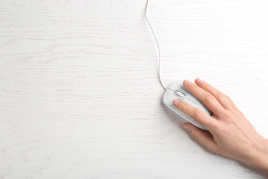 Photo of Woman using modern wired optical mouse on white wooden table, top view. Space for text