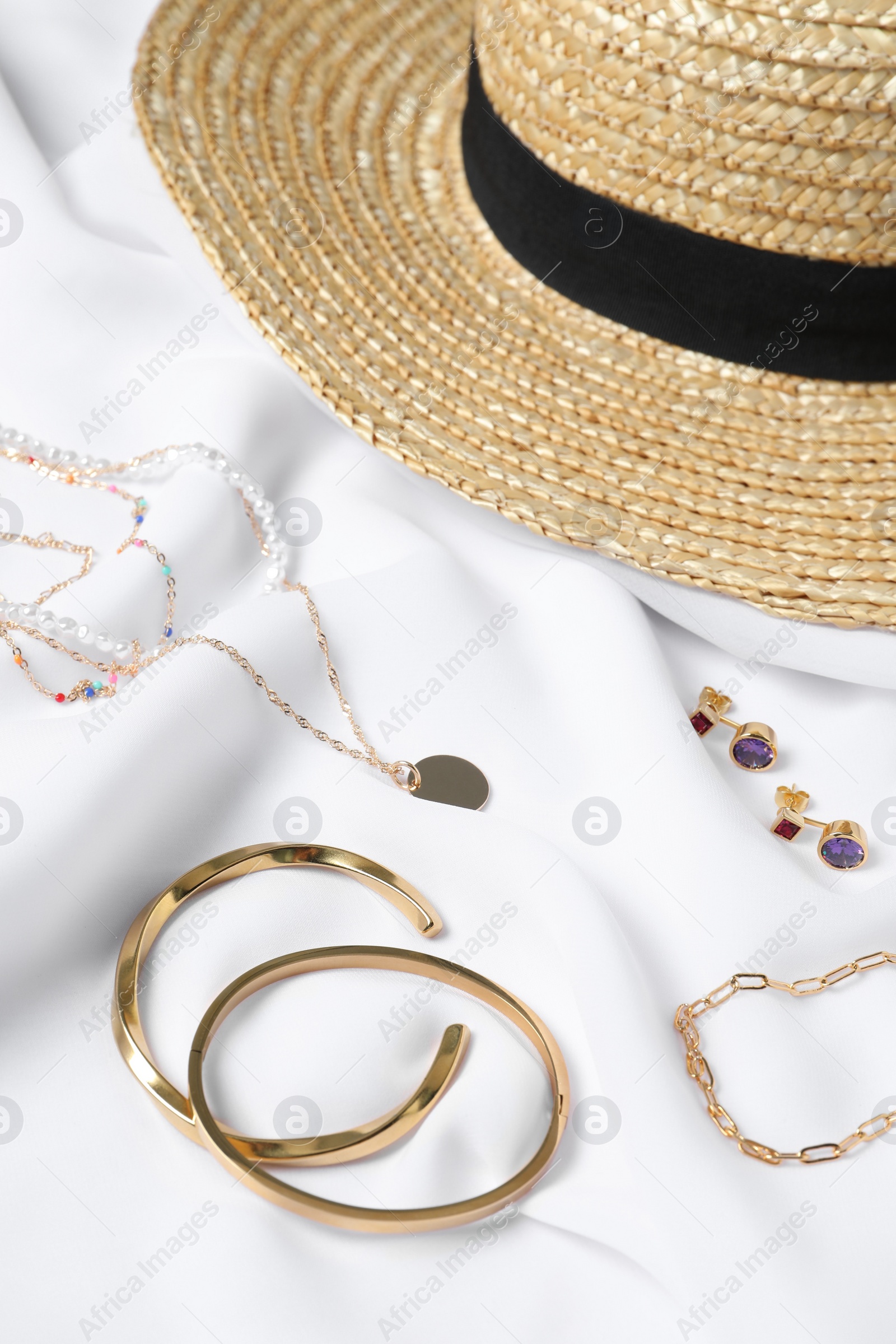 Photo of Different elegant bijouterie and hat on white cloth