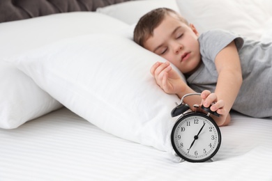 Photo of Cute boy turning off alarm clock in bed, space for text. Healthy sleep