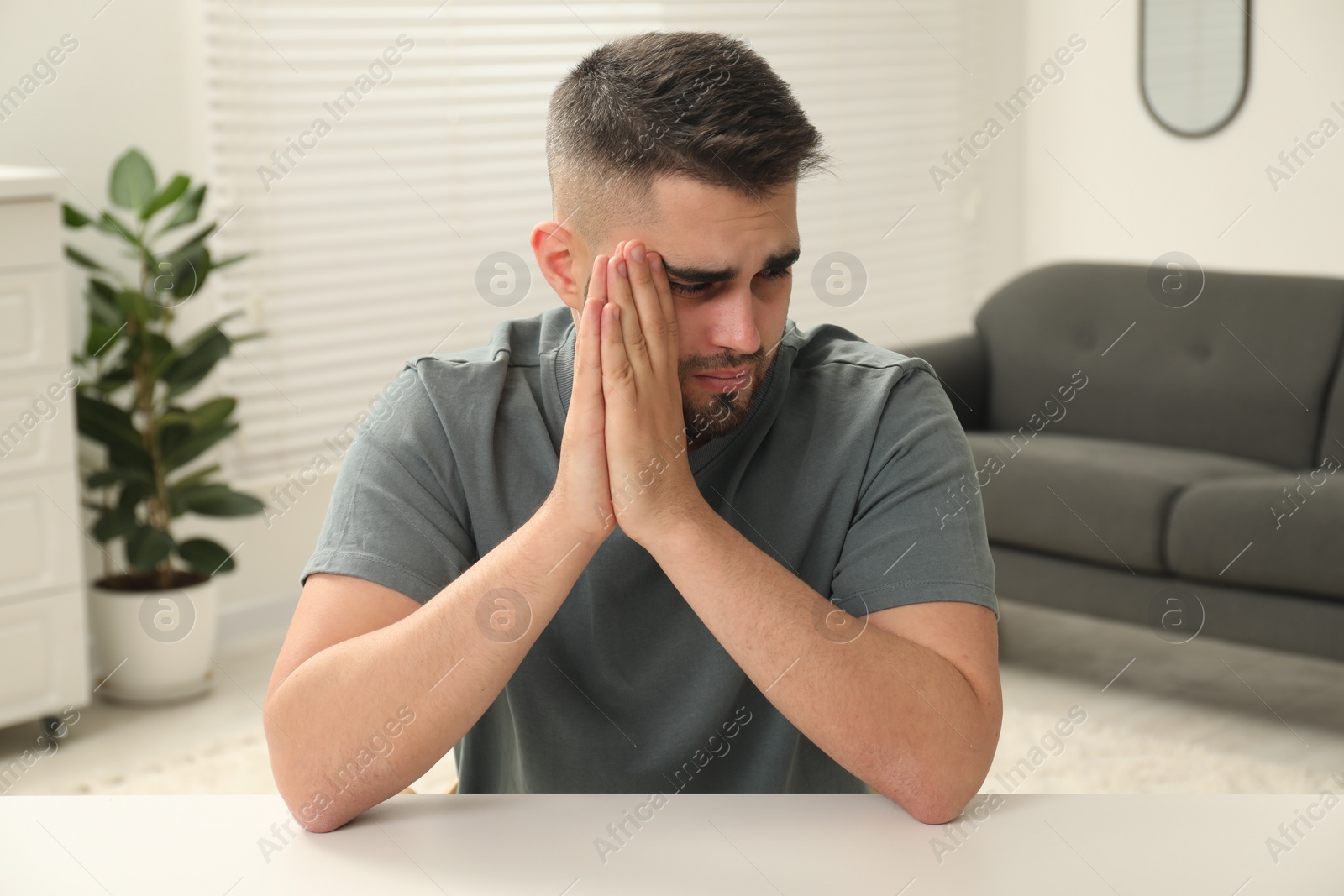 Photo of Sad man sitting at white table indoors