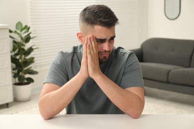 Photo of Sad man sitting at white table indoors