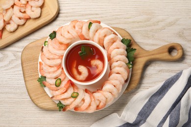 Photo of Tasty boiled shrimps with cocktail sauce, chili and parsley on light wooden table, flat lay