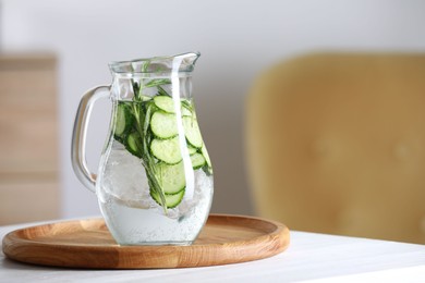 Refreshing cucumber water with rosemary in jug on white table. Space for text