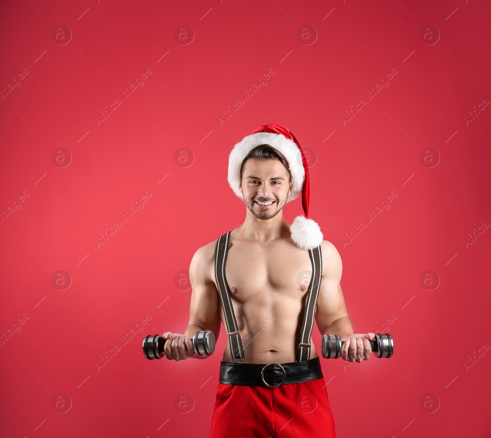 Photo of Shirtless sexy young Santa Claus with dumbbells on color background