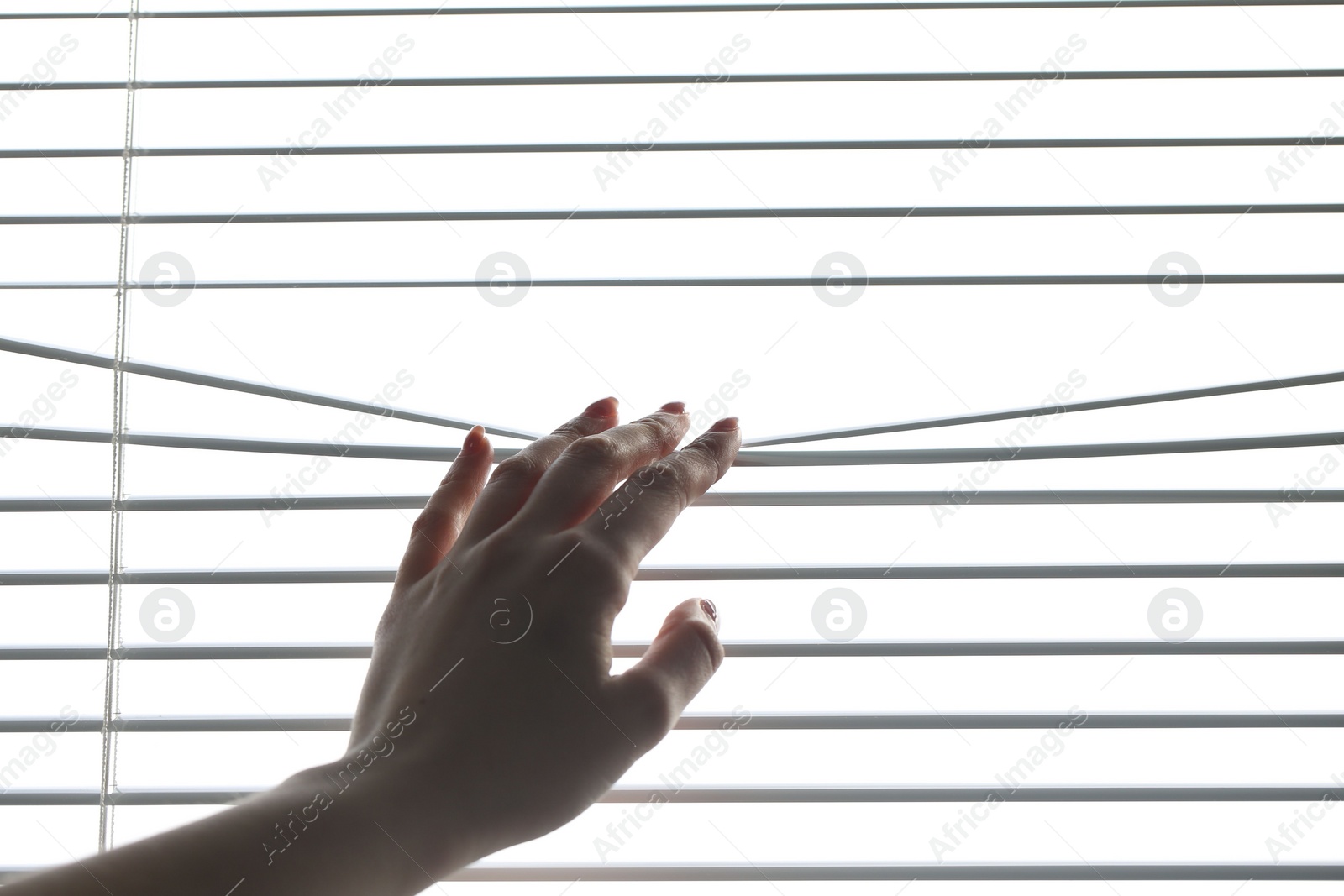 Photo of Woman separating slats of white blinds indoors, closeup