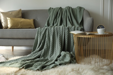 Photo of Stylish room interior with comfortable sofa, knitted blanket and coffee table near white wall