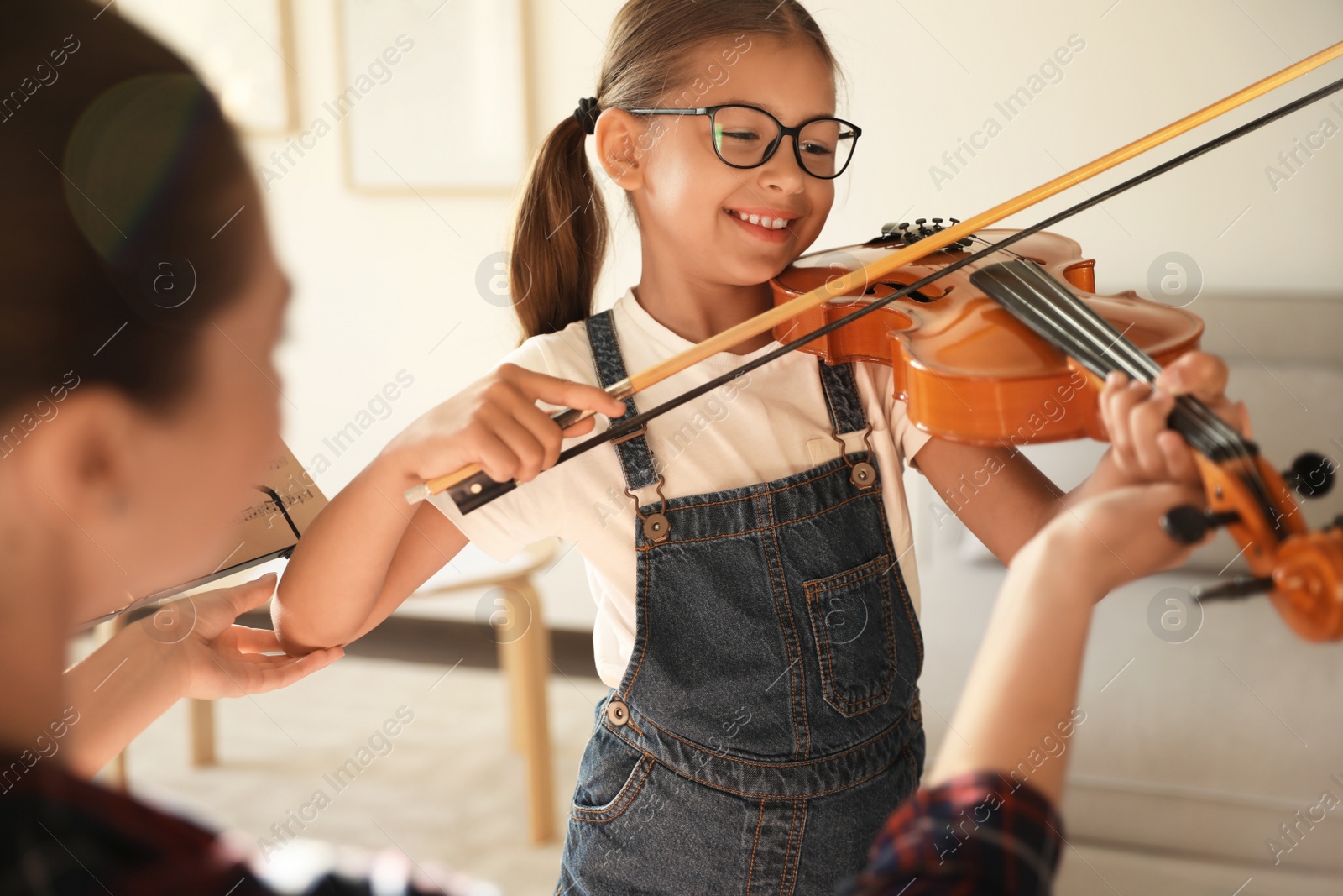 Photo of Young woman teaching little girl to play violin indoors