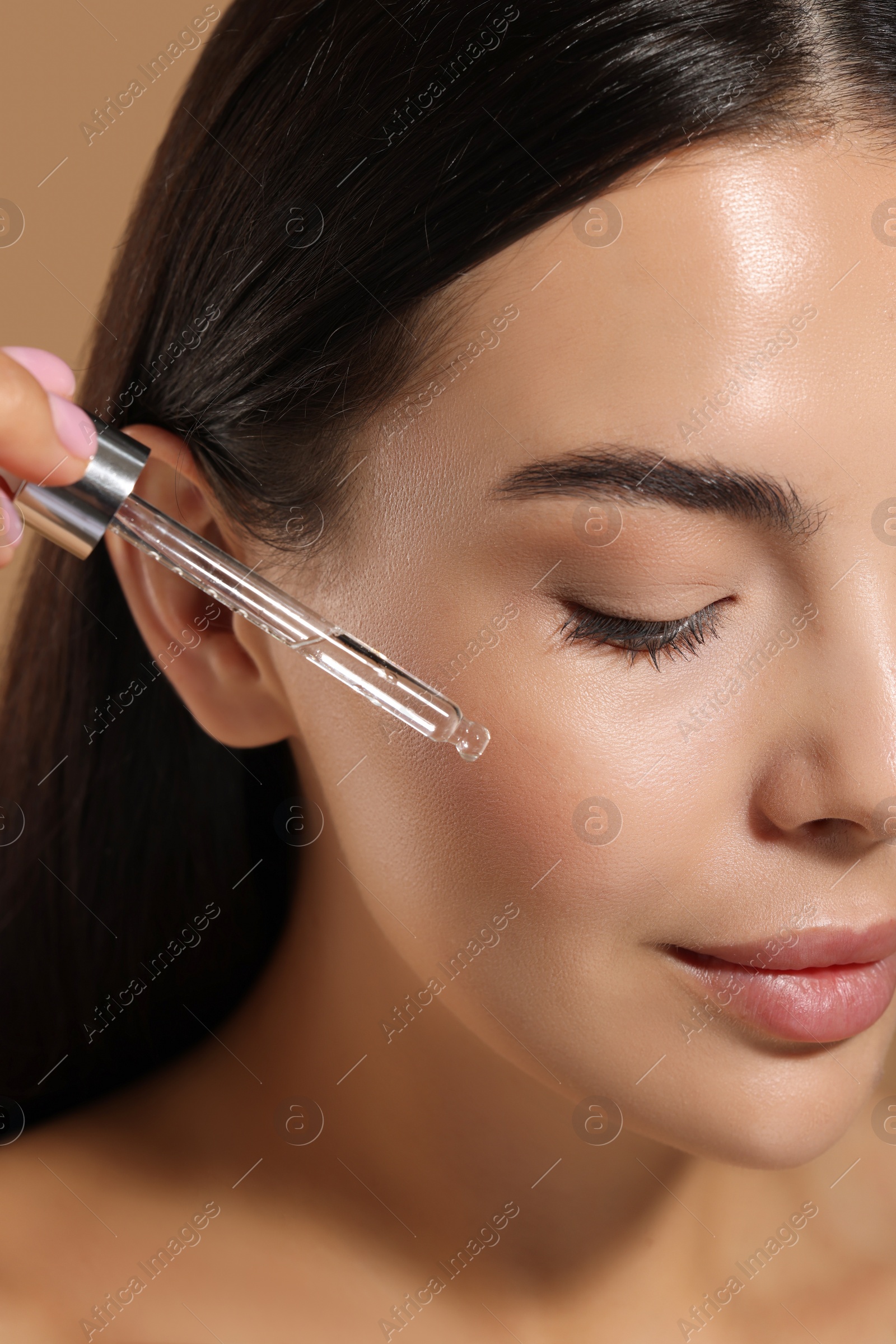 Photo of Beautiful young woman applying serum onto her face on beige background, closeup