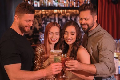Photo of Happy friends clinking glasses with fresh cocktails in bar