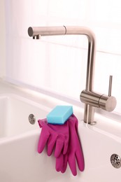 Photo of Sponge and rubber gloves on kitchen sink indoors