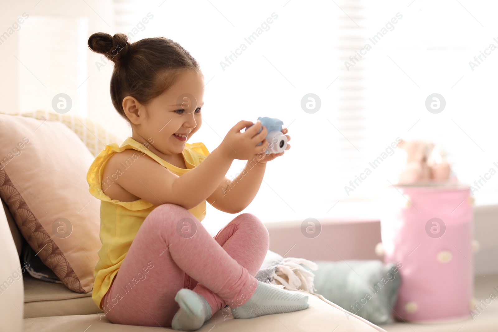 Photo of Little photographer taking picture with toy camera on sofa at home. Space for text