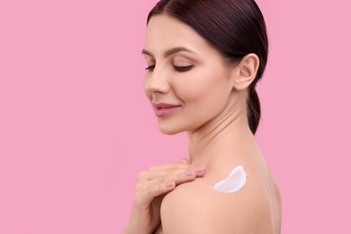 Beautiful woman with smear of body cream on her shoulder against pink background. Space for text