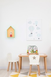 Photo of Table and chairs with toys near white wall in playroom. Stylish kindergarten interior