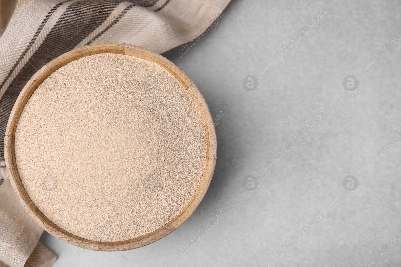 Photo of Granulated yeast in wooden bowl on light gray table, top view. Space for text