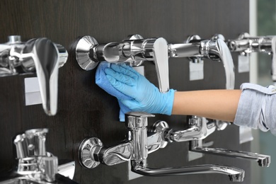 Woman cleaning faucets with rag in bathroom fixtures store, closeup