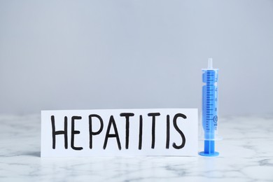 Photo of Word Hepatitis and syringe on white marble table