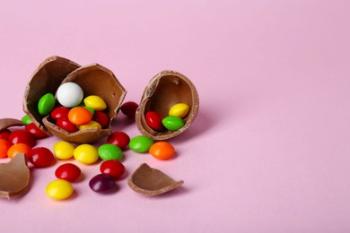 Photo of Broken chocolate egg with colorful candies on pink background. Space for text