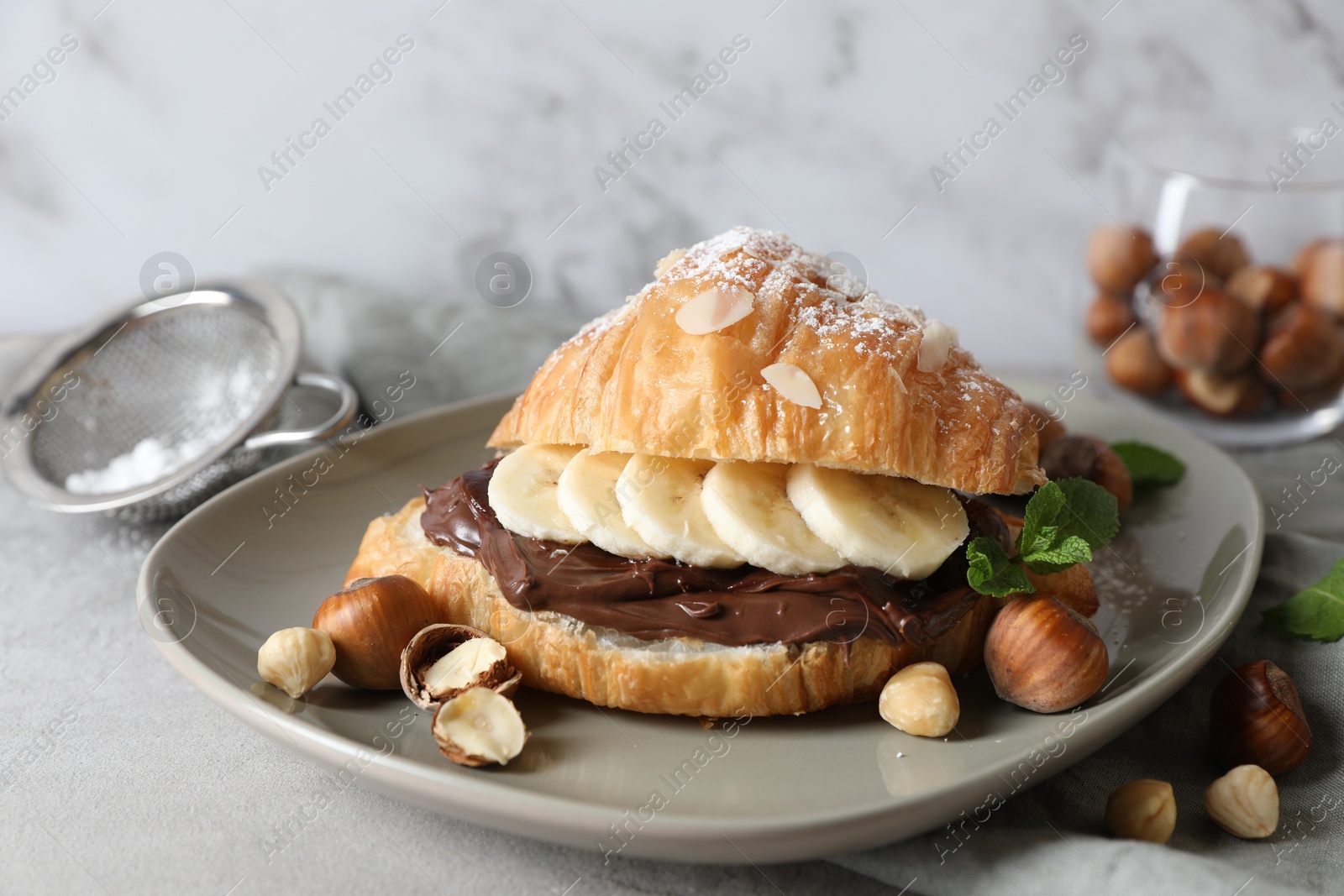 Delicious croissant with banana, chocolate and hazelnuts on gray table, closeup Photo of Delicious croissant with banana, chocolate and hazelnuts on gray table, closeup