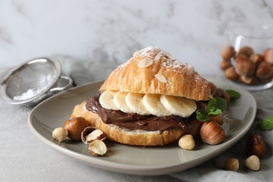 Photo of Delicious croissant with banana, chocolate and hazelnuts on gray table, closeup