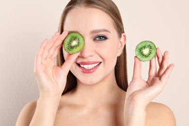 Young woman with cut kiwi on beige background. Vitamin rich food