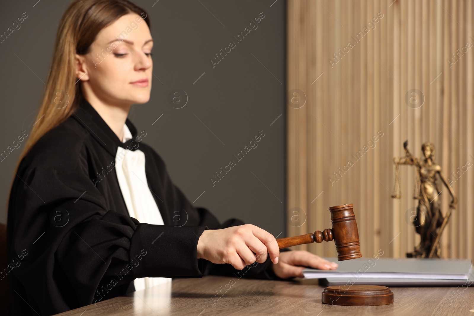 Photo of Judge striking mallet at wooden table in courtroom, selective focus. Space for text