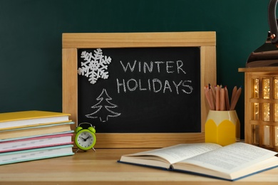 Photo of Chalkboard with text Winter Holidays and school supplies on wooden table