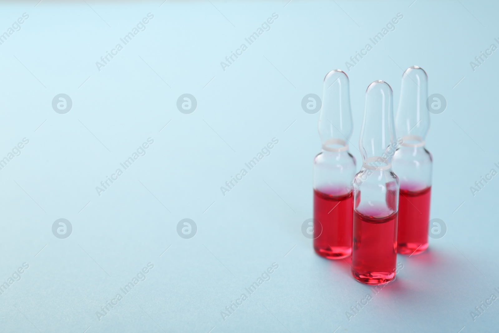 Photo of Glass ampoules with liquid on light blue background. Space for text