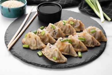 Photo of Delicious gyoza (asian dumplings) with green onions, soy sauce and chopsticks on white table